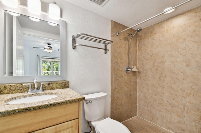 bathroom featuring ceiling fan, tiled shower, a textured ceiling, vanity with extensive cabinet space, and toilet