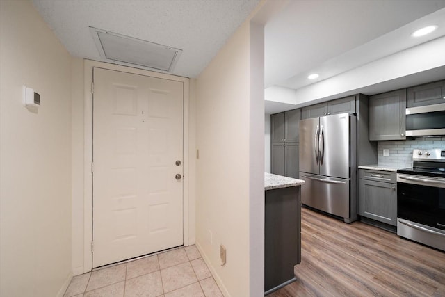 kitchen featuring light stone countertops, gray cabinetry, appliances with stainless steel finishes, light wood-type flooring, and tasteful backsplash