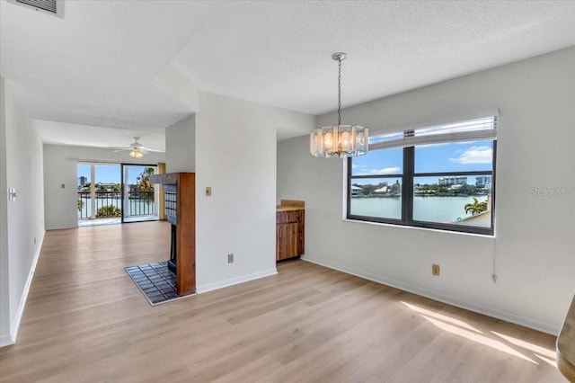 unfurnished dining area featuring a textured ceiling, a water view, light hardwood / wood-style floors, and ceiling fan with notable chandelier