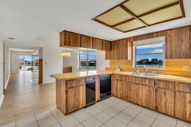 kitchen with kitchen peninsula, backsplash, ceiling fan with notable chandelier, sink, and light hardwood / wood-style flooring