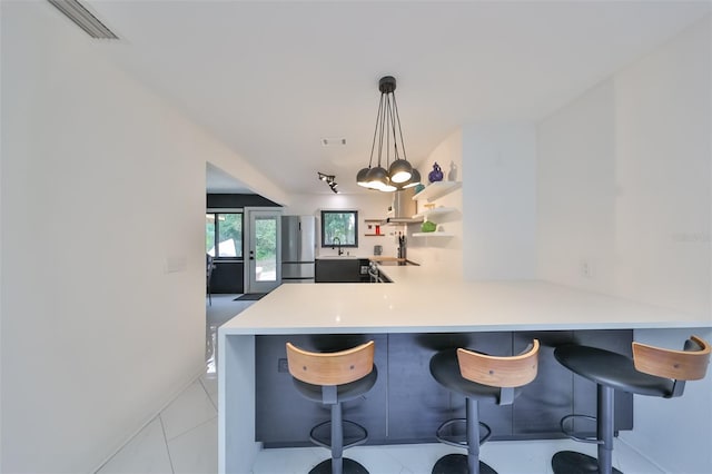 kitchen with pendant lighting, light tile patterned floors, a kitchen bar, kitchen peninsula, and stainless steel refrigerator