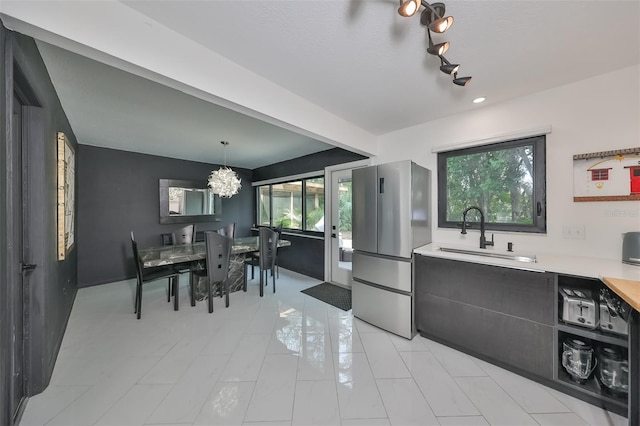 kitchen featuring pendant lighting, sink, light tile patterned flooring, stainless steel refrigerator, and a chandelier