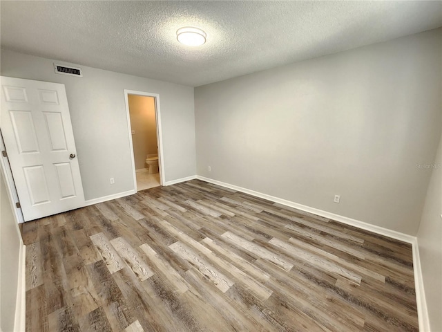 unfurnished bedroom featuring ensuite bath, wood-type flooring, and a textured ceiling