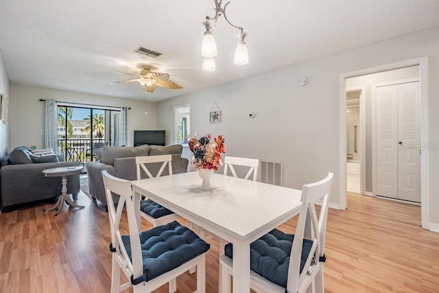 dining area with light hardwood / wood-style floors and ceiling fan with notable chandelier