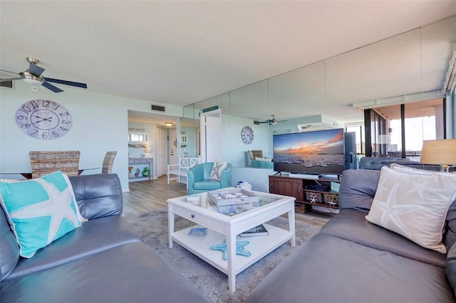 living room featuring wood-type flooring, a textured ceiling, and ceiling fan