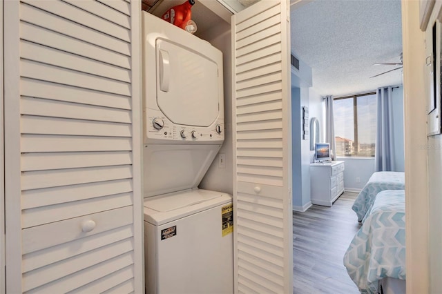 clothes washing area featuring hardwood / wood-style flooring, stacked washer and dryer, and a textured ceiling