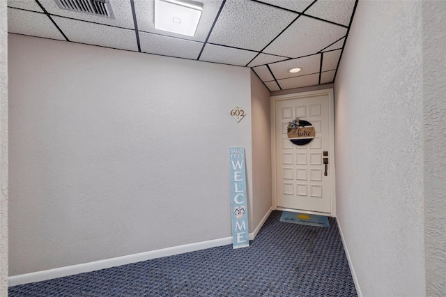 interior space featuring a textured wall, a drop ceiling, visible vents, baseboards, and dark colored carpet