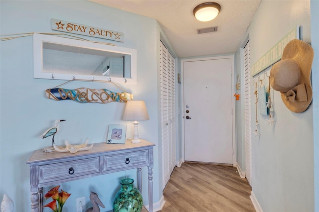 doorway with light wood-type flooring, visible vents, baseboards, and a textured ceiling