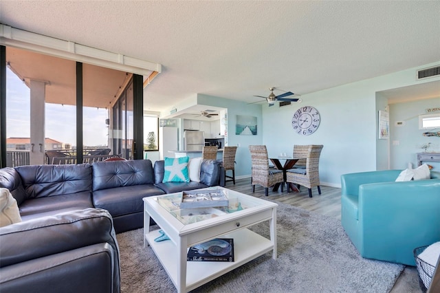 living area featuring visible vents, a textured ceiling, wood finished floors, baseboards, and ceiling fan