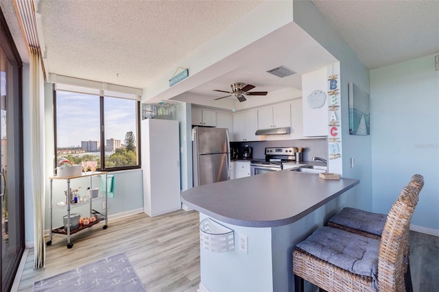 kitchen with visible vents, a peninsula, light wood-style flooring, a sink, and stainless steel appliances