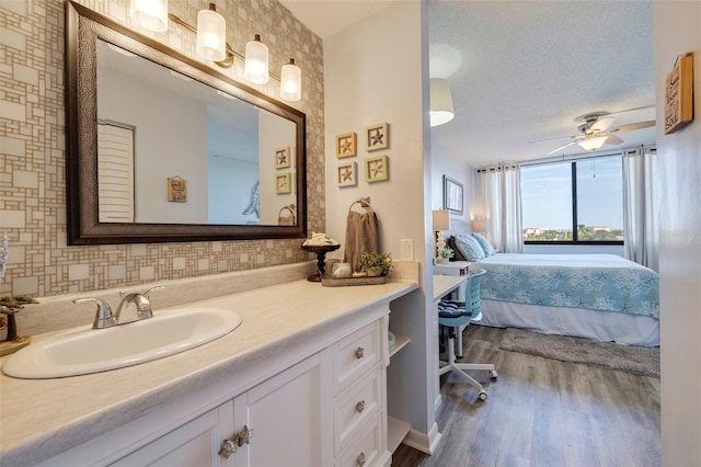 bathroom with a textured ceiling, wood finished floors, ensuite bath, ceiling fan, and vanity