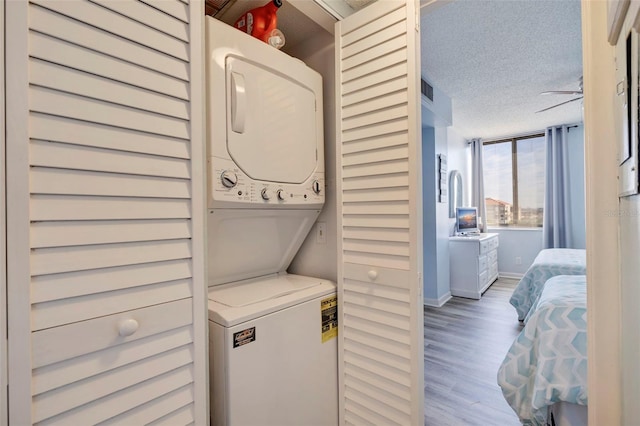 clothes washing area with baseboards, laundry area, stacked washing maching and dryer, light wood-style floors, and a textured ceiling