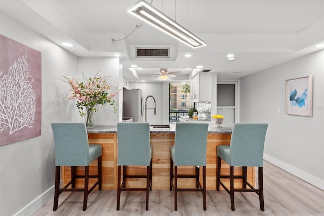 kitchen with stainless steel fridge, light hardwood / wood-style floors, ceiling fan, and a breakfast bar area