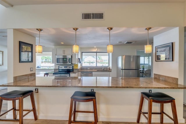 kitchen featuring appliances with stainless steel finishes, kitchen peninsula, a kitchen bar, and white cabinets