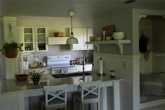 kitchen featuring decorative backsplash, white electric range oven, white cabinetry, hanging light fixtures, and a breakfast bar area