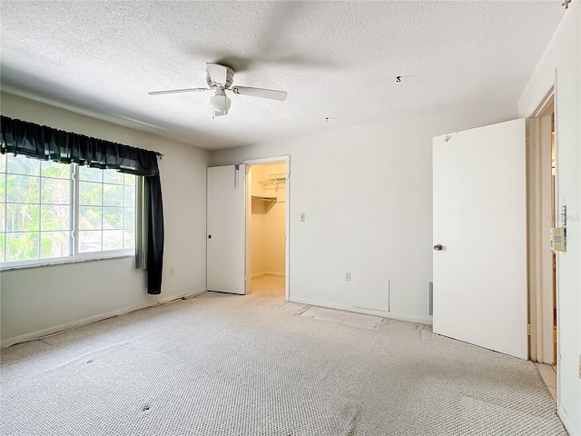 unfurnished bedroom with light colored carpet, a spacious closet, a closet, ceiling fan, and a textured ceiling