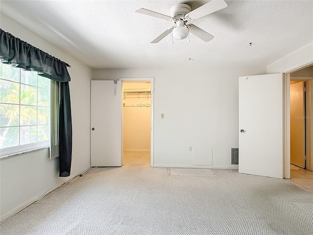 unfurnished bedroom featuring light colored carpet, a closet, ceiling fan, a textured ceiling, and a walk in closet