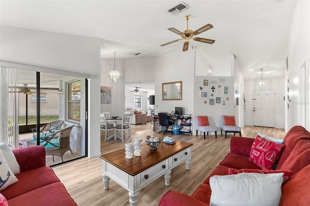 living room with plenty of natural light, high vaulted ceiling, ceiling fan with notable chandelier, and light wood-type flooring