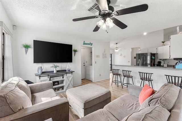 living room featuring a textured ceiling, ceiling fan, and light hardwood / wood-style flooring