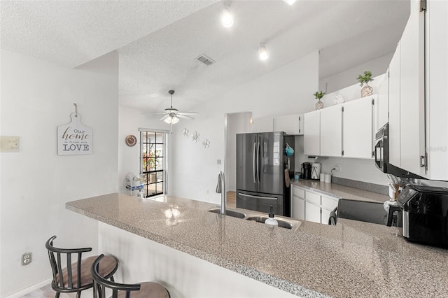 kitchen with stainless steel refrigerator, ceiling fan, kitchen peninsula, light stone countertops, and white cabinets