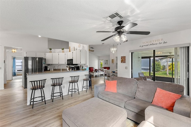 living room featuring light hardwood / wood-style floors, a textured ceiling, ceiling fan with notable chandelier, and a wealth of natural light