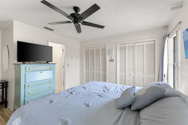 bedroom featuring two closets, a textured ceiling, ceiling fan, and light hardwood / wood-style flooring