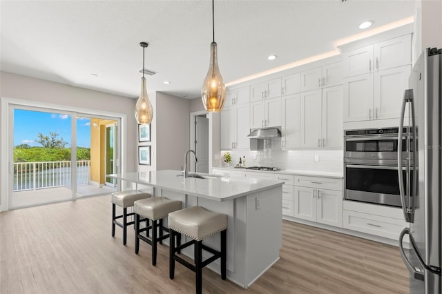 kitchen with white cabinetry, a center island with sink, hanging light fixtures, and sink