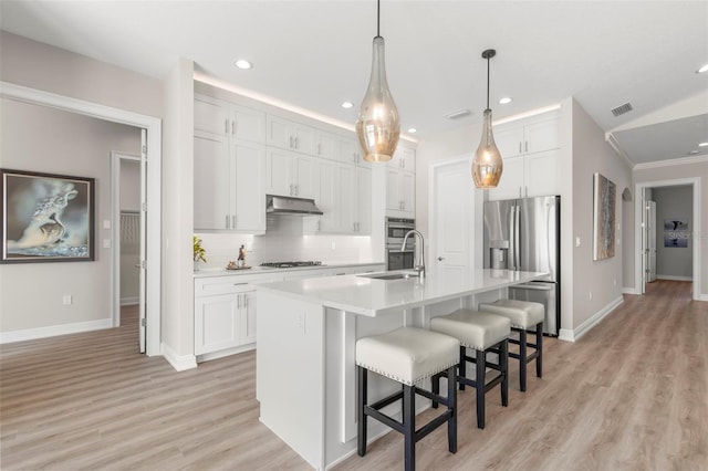 kitchen with pendant lighting, white cabinets, stainless steel appliances, a kitchen island with sink, and vaulted ceiling