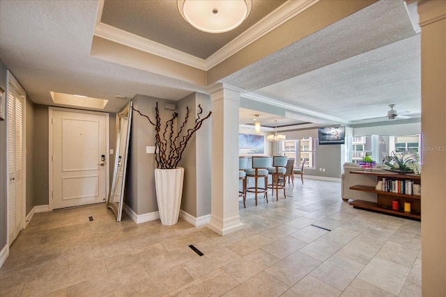 entrance foyer featuring ceiling fan, light tile floors, a tray ceiling, ornamental molding, and ornate columns