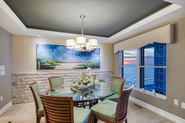 dining room featuring a water view, a tray ceiling, light tile flooring, and a chandelier