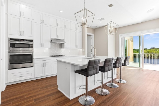 kitchen with stainless steel double oven, dark hardwood / wood-style flooring, white cabinets, and tasteful backsplash