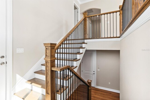 stairway with dark hardwood / wood-style flooring, crown molding, and a towering ceiling