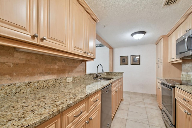 kitchen with stainless steel appliances, backsplash, light tile floors, sink, and light stone countertops