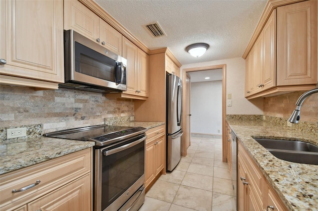 kitchen featuring tasteful backsplash, light tile floors, stainless steel appliances, light stone countertops, and sink