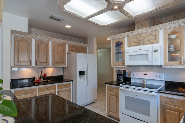 kitchen with dark stone countertops, light brown cabinetry, white appliances, light tile patterned flooring, and tasteful backsplash