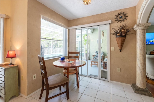 tiled dining space featuring a textured ceiling, a healthy amount of sunlight, and ornate columns