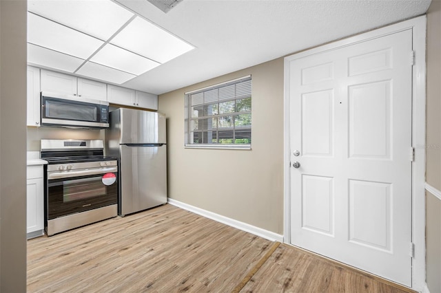 kitchen with appliances with stainless steel finishes, light hardwood / wood-style floors, and white cabinets