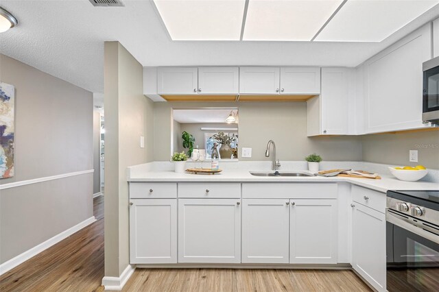 kitchen featuring appliances with stainless steel finishes, light hardwood / wood-style flooring, sink, and white cabinetry