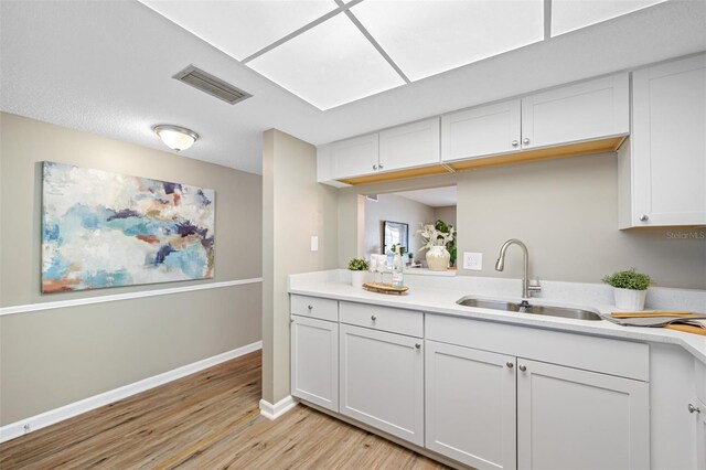 kitchen with white cabinets, light hardwood / wood-style flooring, and sink