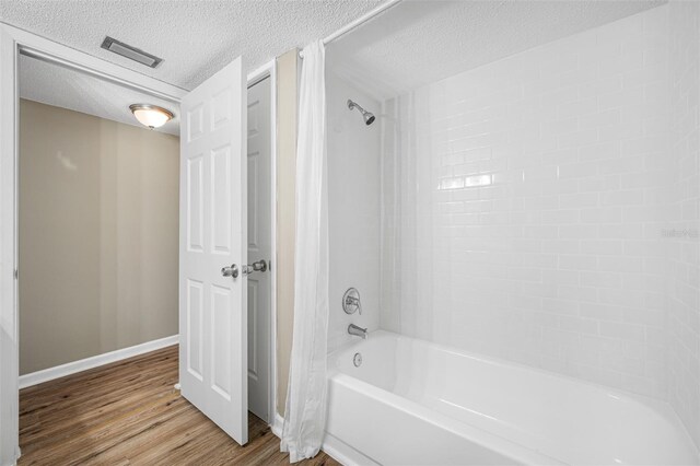 bathroom with a textured ceiling, shower / bathing tub combination, and hardwood / wood-style flooring