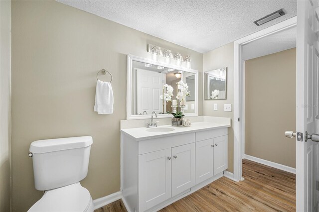 bathroom with hardwood / wood-style flooring, toilet, vanity, and a textured ceiling