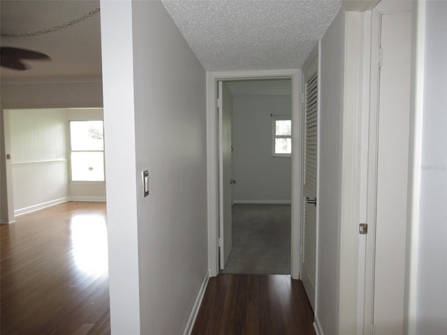 corridor with dark wood-type flooring, a textured ceiling, and baseboards