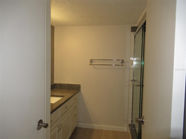 full bathroom featuring a shower with shower door, a textured ceiling, baseboards, and vanity