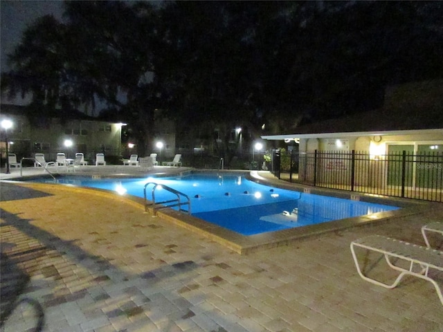 pool at night with a patio area, a community pool, and fence