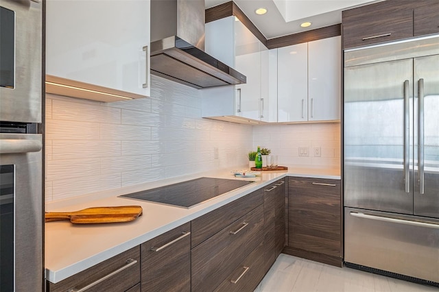 kitchen with tasteful backsplash, dark brown cabinets, white cabinetry, stainless steel built in fridge, and wall chimney exhaust hood