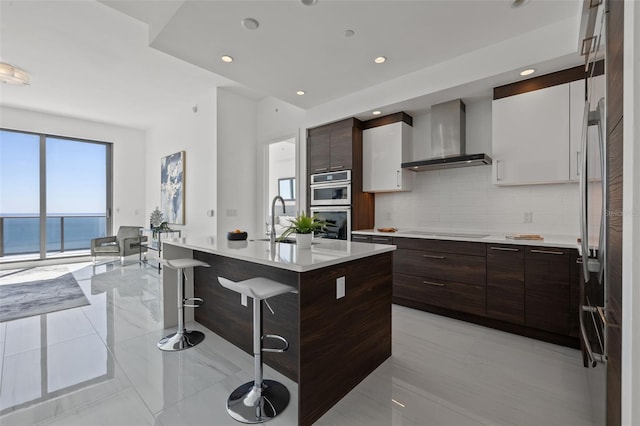 kitchen with white cabinets, light tile flooring, a breakfast bar area, wall chimney exhaust hood, and tasteful backsplash