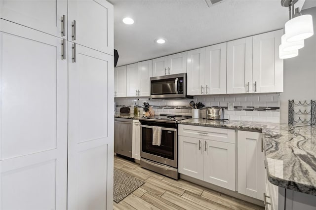 kitchen with appliances with stainless steel finishes, backsplash, decorative light fixtures, white cabinetry, and light stone countertops