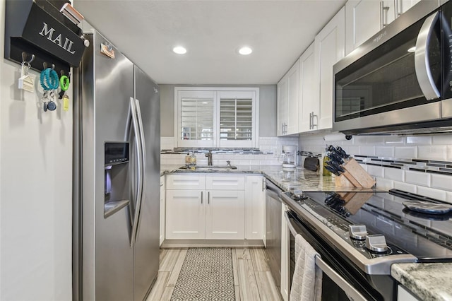 kitchen with appliances with stainless steel finishes, light hardwood / wood-style floors, sink, light stone countertops, and white cabinets