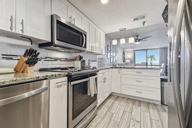 kitchen featuring light stone counters, tasteful backsplash, white cabinetry, stainless steel appliances, and kitchen peninsula