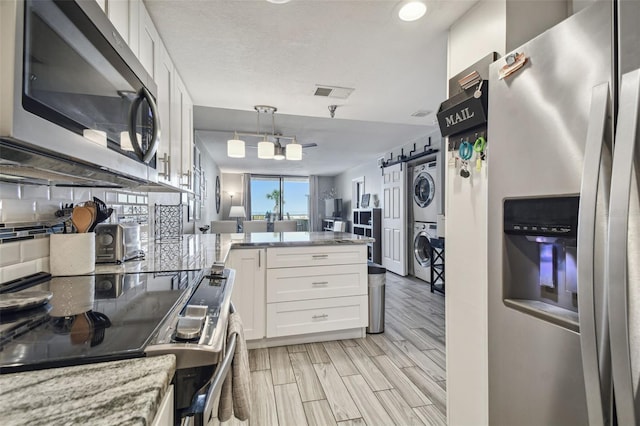 kitchen with appliances with stainless steel finishes, pendant lighting, light hardwood / wood-style flooring, white cabinetry, and stacked washer / drying machine